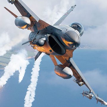 First image shows a middle-aged Asian man with short dark hair wearing a dark suit white shirt and blue tie standing at a podium with microphones against a backdrop of red flags with yellow stars and a blue flag. Second image depicts a sleek gray fighter jet with orange accents flying low over blue water with white clouds in the sky emitting white contrails from its engines and carrying cylindrical missiles under its wings.