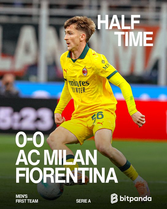 A male soccer player with blonde hair wearing a yellow AC Milan away jersey with number 16 and sponsor logos including Puma and Emirates dribbles a ball on a green grass field during a match with stadium seating and advertising boards in the blurred background including Bitpanda logo. Overlaid text reads HALF TIME in large white letters at the top 0-0 score in red and black at the bottom AC MILAN FIORENTINA in bold fonts Mens First Team Serie A at the base.