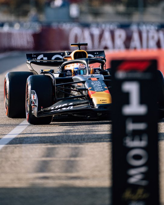 Formula 1 race car driven by Max Verstappen of Red Bull Racing team speeds on the track during the United States Grand Prix. The car features blue and red livery with sponsor logos including Oracle and Red Bull. Trackside barriers and advertising boards for Moet and Chandon are visible in the foreground and background. Other cars and spectators appear in the distance under a partly cloudy sky.