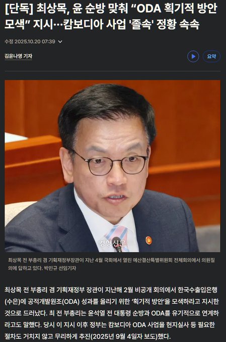 A formal indoor setting shows a middle-aged Korean man with short black hair and glasses wearing a dark suit, white shirt, and tie, seated at a wooden table with microphones, documents, and nameplates including ODA, during what appears to be an official meeting or press event.