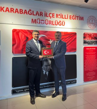 First image displays a formal office setting with a wall sign reading Karabağlar İlçe Milli Eğitim Müdürlüğü, two men in dark suits standing side by side holding a small Turkish flag framed by red borders, one man with glasses and the other with a mustache, behind them Turkish flags and educational plaques including a portrait of Mustafa Kemal Atatürk and text about education and teachers, red and white color scheme dominant. Second image shows five men in formal attire including suits and one in a casual jacket gathered in the same office space under the Karabağlar İlçe Milli Eğitim Müdürlüğü sign, two central figures holding a Turkish flag, others standing nearby with serious expressions, background features Turkish flags, a large Atatürk portrait, and informational panels in Turkish about education initiatives.