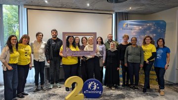 First image shows a large group of adults mostly wearing yellow shirts and some in casual attire standing together in a modern conference room with large windows and a purple backdrop featuring the eTwinning logo, holding a large photo frame of similar group pose, and a large number 2 with eTwinning emblem on the floor in front. Second image depicts a colorful classroom scene with children in orange and yellow shirts sitting at orange desks, holding flags and toys, surrounded by adults in various outfits, with blue balloons, educational posters on walls, and storage cabinets filled with supplies. Third image captures a diverse group of adults in coats and scarves posing together in a school hallway with beige walls, a framed portrait, and a banner in Turkish reading something like Ministry of National Education, near wooden doors. Fourth image presents several women in yellow tops standing on a stage area leading a presentation, gesturing towards a projector screen displaying collaborative learning graphics and eTwinning elements, with tables chairs and laptops in a green-walled meeting room.