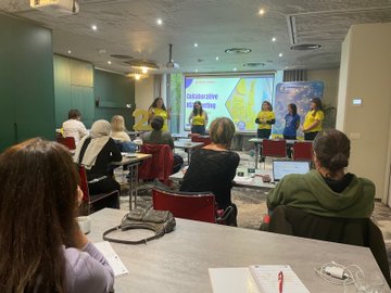 First image shows a large group of adults mostly wearing yellow shirts and some in casual attire standing together in a modern conference room with large windows and a purple backdrop featuring the eTwinning logo, holding a large photo frame of similar group pose, and a large number 2 with eTwinning emblem on the floor in front. Second image depicts a colorful classroom scene with children in orange and yellow shirts sitting at orange desks, holding flags and toys, surrounded by adults in various outfits, with blue balloons, educational posters on walls, and storage cabinets filled with supplies. Third image captures a diverse group of adults in coats and scarves posing together in a school hallway with beige walls, a framed portrait, and a banner in Turkish reading something like Ministry of National Education, near wooden doors. Fourth image presents several women in yellow tops standing on a stage area leading a presentation, gesturing towards a projector screen displaying collaborative learning graphics and eTwinning elements, with tables chairs and laptops in a green-walled meeting room.