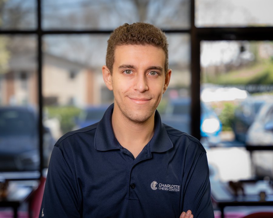 Portrait of young man with short curly hair smiling slightly wearing navy polo shirt with Charlotte Chess Center logo on chest standing indoors near large windows overlooking parking lot and buildings. Second image shows formal letter on white paper with center logo at top titled Official Statement from the Naroditsky Family dated October 2025 expressing sadness over Daniel Naroditskys unexpected passing describing him as talented chess player commentator educator and beloved community member requesting privacy for family during grief and remembering his passion inspiration to players worldwide with logo at bottom.