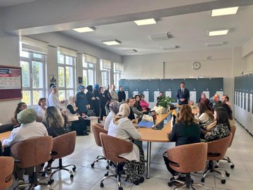 First image shows a group of women in headscarves and professional attire seated around a conference table in a bright classroom with windows and cabinets, engaged in discussion with a man standing and speaking. Second image depicts a man in a suit standing and addressing female students in headscarves seated at wooden desks in a classroom with white curtains and windows. Third image captures a diverse group of male and female students and staff, some in headscarves, standing together in a classroom near desks and a whiteboard. Fourth image features five individuals, including men in suits and women in headscarves, posing in front of a school building entrance with signage for Pen Sosyal Kulup Anadolu Imam Hatip Lisesi.