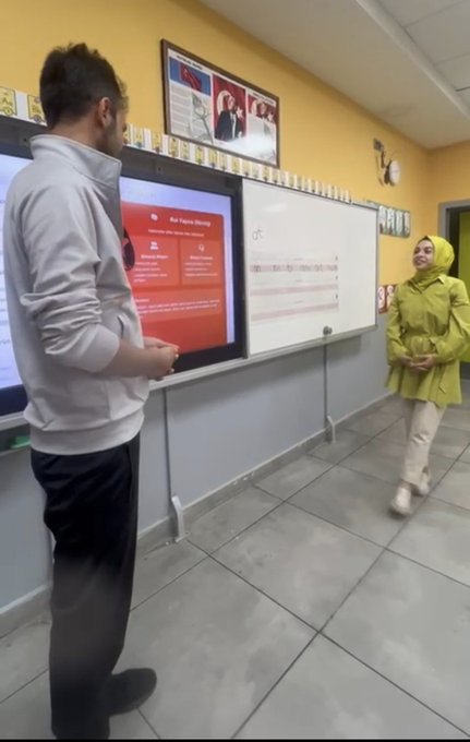 First image shows a training room with participants seated at computers around tables listening to a standing facilitator near a large screen displaying educational content. Second image depicts a classroom with two women facing a projector screen showing text about digital media literacy while a male instructor stands nearby. Third image features a group of diverse participants including men and women some wearing headscarves sitting at tables with laptops and engaging in a session with colorful quadrants on a screen. Fourth image captures a male instructor in a yellow classroom pointing at a smartboard displaying a red interface with user profiles while a female participant in a green raincoat stands attentively nearby.