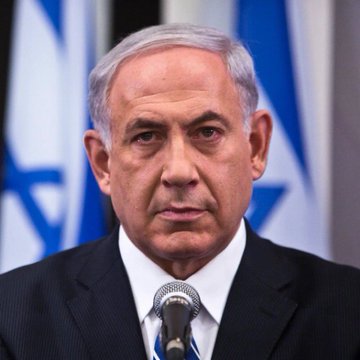 First image shows an older man with gray hair and glasses wearing a black leather jacket leaning against a tree trunk in an outdoor setting with blurred trees in the background. Second image depicts an older man with gray hair in a dark suit standing at a podium with a microphone speaking with two Israeli flags positioned behind him.