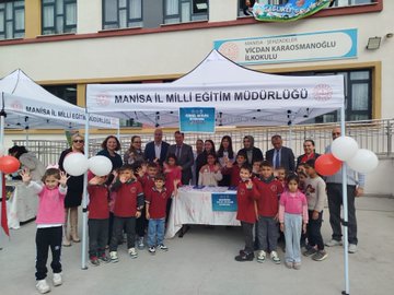 First image shows a group of adults and children standing together under a white tent labeled Manisa İl Milli Eğitim Müdürlüğü outside a school building with yellow walls and a sign for Vicdan Karaosmanoğlu school children wearing red uniforms holding balloons and standing around a table with papers. Second image depicts teenage girls in red uniforms holding blue signs that say something about health under another white tent with tables covered in colorful game boards and stacks of brochures near a school railing. Third image features a large group of children mostly in pink and red clothing gathered around a white tent outside the school entrance with a blue banner and trash bin visible in the background. Fourth image displays children in school uniforms including red polo shirts interacting with a large pink tooth model and toothbrushes on a white table covered with health logos and stacks of books under the tent.