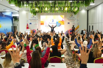 First image shows two side-by-side photos of men in suits speaking at podiums with eTwinning banners Turkish and EU flags and floral decorations in a conference room. Second image depicts a large group of diverse attendees mostly women in professional attire seated at red-covered tables in a spacious venue with blue eTwinning banner hanging plants and a stage. Third image captures an audience raising hands in applause during a presentation with eTwinning logos on screens Turkish flag and colorful banners in a hall with seated participants. Fourth image features a woman presenting at a podium with eTwinning and Together We Shine banners Turkish and EU flags projector screen showing text and attendees seated at tables in a decorated room.