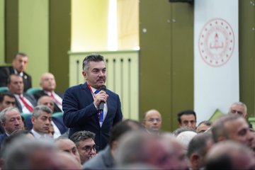 First image displays a conference stage with large screens showing Turkish flags and text İLÇE MİLLİ EĞİTİM MÜDÜRLERİ TOPLANTISI backdrop featuring portraits of suited men one speaking at podium with microphone flowers on table audience of men in suits seated in rows chairs and projector screen visible. Second image shows wide view of auditorium with green walls lighting rigs large portrait of suited man with Turkish flag audience of men and women in formal attire seated in rows speaker at table with microphone flowers and documents on stage. Third image focuses on man in dark suit with red lanyard holding microphone speaking to audience of men in suits seated in green chairs backdrop with blurred stage elements. Fourth image depicts man in suit with lanyard holding microphone speaking audience of men in suits seated behind him green wall with red emblem and Arabic script visible.