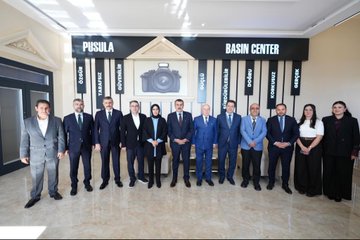 First image shows a group of people including men in suits and women in headscarves standing and viewing a wall covered with framed newspaper clippings and headlines in Turkish, such as Pusula and Yurttan, inside a modern indoor space with beige walls and large windows. Second image depicts a formal meeting around a wooden table with red folders, where several individuals including Yusuf Tekin in a suit sit with women in headscarves and professional attire, Turkish flags and another flag present, and a banner reading Pusula Gazetesi. Third image features a large group of about 15 professionals in suits and modest clothing posing together in front of a sign reading Pusula Basin Merkezi with a camera icon, in an elegant hall with arched ceiling and decorative elements.