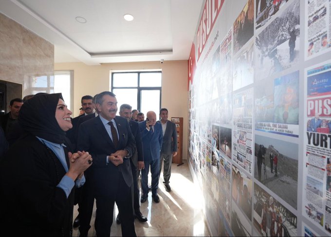 First image shows a group of people including men in suits and women in headscarves standing and viewing a wall covered with framed newspaper clippings and headlines in Turkish, such as Pusula and Yurttan, inside a modern indoor space with beige walls and large windows. Second image depicts a formal meeting around a wooden table with red folders, where several individuals including Yusuf Tekin in a suit sit with women in headscarves and professional attire, Turkish flags and another flag present, and a banner reading Pusula Gazetesi. Third image features a large group of about 15 professionals in suits and modest clothing posing together in front of a sign reading Pusula Basin Merkezi with a camera icon, in an elegant hall with arched ceiling and decorative elements.