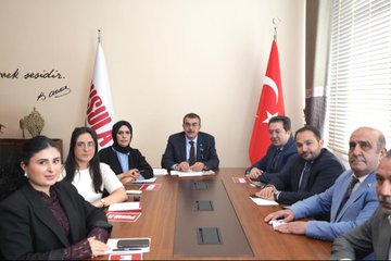 First image shows a group of people including men in suits and women in headscarves standing and viewing a wall covered with framed newspaper clippings and headlines in Turkish, such as Pusula and Yurttan, inside a modern indoor space with beige walls and large windows. Second image depicts a formal meeting around a wooden table with red folders, where several individuals including Yusuf Tekin in a suit sit with women in headscarves and professional attire, Turkish flags and another flag present, and a banner reading Pusula Gazetesi. Third image features a large group of about 15 professionals in suits and modest clothing posing together in front of a sign reading Pusula Basin Merkezi with a camera icon, in an elegant hall with arched ceiling and decorative elements.