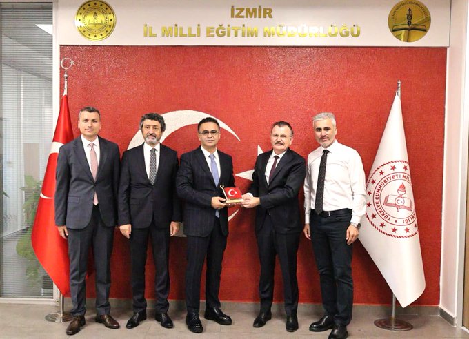 First image displays two men in dark suits shaking hands with plaques reading İl Milli Eğitim Müdürlüğü on a red wall flanked by Turkish flags and a white flag with a red emblem. Second image shows five men in suits including the two from the first image exchanging a document or plaque in the same formal setting with additional participants wearing ties and professional attire against the institutional backdrop with golden emblems.