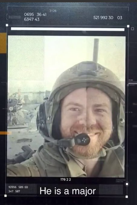 Selfie of a bearded man with smiling expression wearing military helmet and gear in a dusty outdoor setting with blurred background structures. Text overlay at bottom reads He is a major.