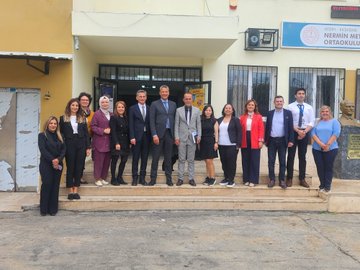 First image shows a large group of about 15-20 adults including men in suits and women in professional attire and headscarves standing in front of a yellow school building with a blue sign reading ORTAOKULU. Second image depicts six adults in business clothes including headscarves posing inside a classroom with a projector screen displaying MEB content and tables. Third image features four adults in formal wear standing on steps in front of a pink and yellow school building with a sign reading ÇANAKKALE MERKEZİ CEVAT PAŞA ORTAOKULU. Fourth image shows a classroom with around 20 students in uniforms seated at desks using laptops while a male teacher in suit stands presenting near a computer screen.