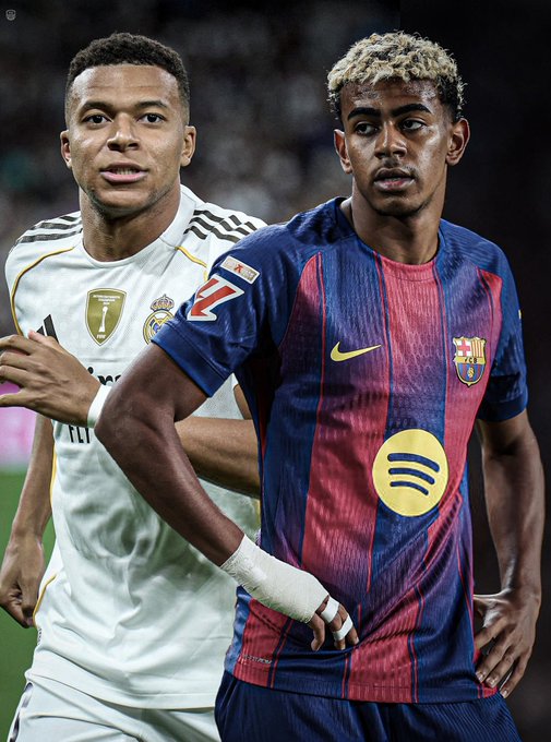 Two soccer players stand on a green field in a stadium under bright lights one with short curly hair wearing a white Real Madrid jersey with gold accents and sponsor logos holding a ball the other with blonde dreadlocks in a blue and red Barcelona kit with Nike and Spotify patches both looking focused with arms extended as if in motion during a match.