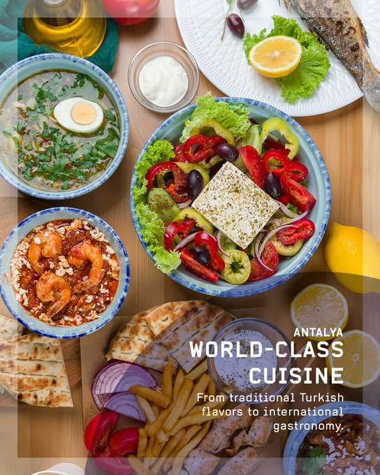 First image displays bold text Antalya Is Waiting For You with details on the 77th International Astronautical Congress as one of the worlds most stunning destinations over a scenic view of Antalya featuring historic buildings a mosque minaret seafront with boats palm trees and a beach promenade. Second image shows Antalya as Turkeys Tourism Capital with text describing it as a hub attracting millions of visitors yearly for culture and events above a panoramic view of the citys historic walls red tower terracotta rooftops greenery and sea. Third image features text Easy To Antalya explaining well-connected via Turkish Airlines flying to more countries than any other airline over an image of a Turkish Airlines airplane in flight against a blue sky. Fourth image presents world-class cuisine from traditional Turkish to international flavors on a wooden table with dishes including green salad with egg olive oil feta cheese tomatoes cucumbers peppers shrimp in tomato sauce yogurt soup grilled fish lemon wedges pita bread olives and french fries.