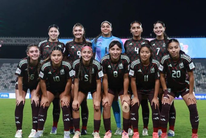 Group of eleven young female soccer players from Mexico in green and white uniforms with numbers like 4 6 8 20 kneeling and standing on a green field at night under stadium lights with a soccer ball held by one player and Adidas branding visible on jerseys.
