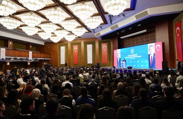 Large conference hall with blue and red banners displaying Turkish flags and text for 2024 YLSY Bursiyerleri Vizyon ve Farkındalık Eğitimi Programı featuring large portraits of Yusuf Tekin at podium with audience seated below stage with microphones and decorative elements second image shows elegant hall with chandeliers wooden panels Turkish flags and suited men including speaker at white podium with flower arrangements third image depicts auditorium with green walls large screen showing event logo audience in chairs and speakers on stage fourth image group photo of diverse professionals in suits and dresses standing in front of blue banner with ministry emblem and Turkish flags