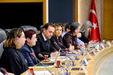 First image shows a long conference table in a modern room with wooden panels and flags including Turkish and Kosovo ones, where numerous professionals in suits sit on both sides engaged in a meeting, with laptops, documents, and a projector visible. Second image depicts a closer view of the meeting table with delegates including men and women in formal attire, microphones, water glasses, notebooks, and a Turkish flag in the background. Third image captures another segment of the table discussion with participants leaning forward, holding microphones, sipping from tea glasses, surrounded by papers and laptops. Fourth image features a large group of about 20 professionals standing in front of the TÜBİTAK building entrance with its logo and Turkish flag, dressed in business suits and dresses on steps with a blue carpet.