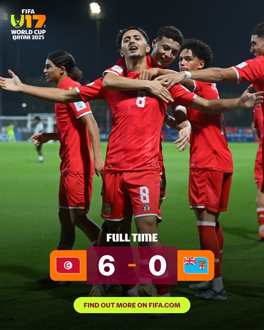 Group of young male soccer players in red jerseys and shorts with white numbers and sponsor logos celebrate a goal on a green grass field under bright stadium floodlights at night. They raise arms, embrace, and smile joyfully, with one player number 8 central. Scoreboard overlay shows full time 6-0 with Morocco flag left and another flag right. FIFA U17 World Cup Qatar 2023 logo top left.