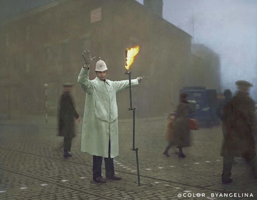 1935, London: A gas-powered flare aides a police officer directing traffic in the London fog. Color_byangelina.