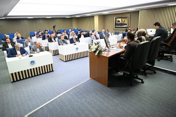 First image shows three men in suits seated at a table with AK Parti Battalgazi Ilce Baskanligi banner behind them including Turkish flags and light bulb logos. Second image depicts a group of men in formal attire seated in red chairs in a meeting room with a podium and documents. Third image features officials at a desk in Battalgazi Belediye Baskanligi setting with Turkish and municipal flags and a woman present. Fourth image illustrates a council session with multiple people around white tables adorned with flowers and microphones in a formal hall.