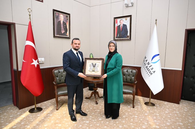 First image shows a man in a dark suit holding a framed green item with a woman in a green coat and headscarf standing beside him in a room with Turkish flags, a white flag, wooden furniture, and portraits on the walls. Second image depicts the same man and woman seated facing each other across a low table with decorative vases and plants in a modern office with flags and shelves. Third image features five professionals in suits and one woman in green attire seated around a glass table in a conference room with display cabinets, awards, and plants visible.