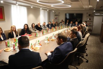 First image shows a long conference table in a modern room with Turkish and organizational flags on walls, multiple professionals in suits seated around the table discussing, water bottles and documents present. Second image depicts two men in suits standing before a wooden wall with gold lettering reading T ürkiye Kamu-Sen, one holding a red-starred plaque in a box. Third image features another conference table setup with Turkish flags, professionals in business attire seated and engaged in meeting, water bottles on table. Fourth image displays a similar conference room scene with large circular light fixture, group of suited individuals around a wooden table with drinks and papers.