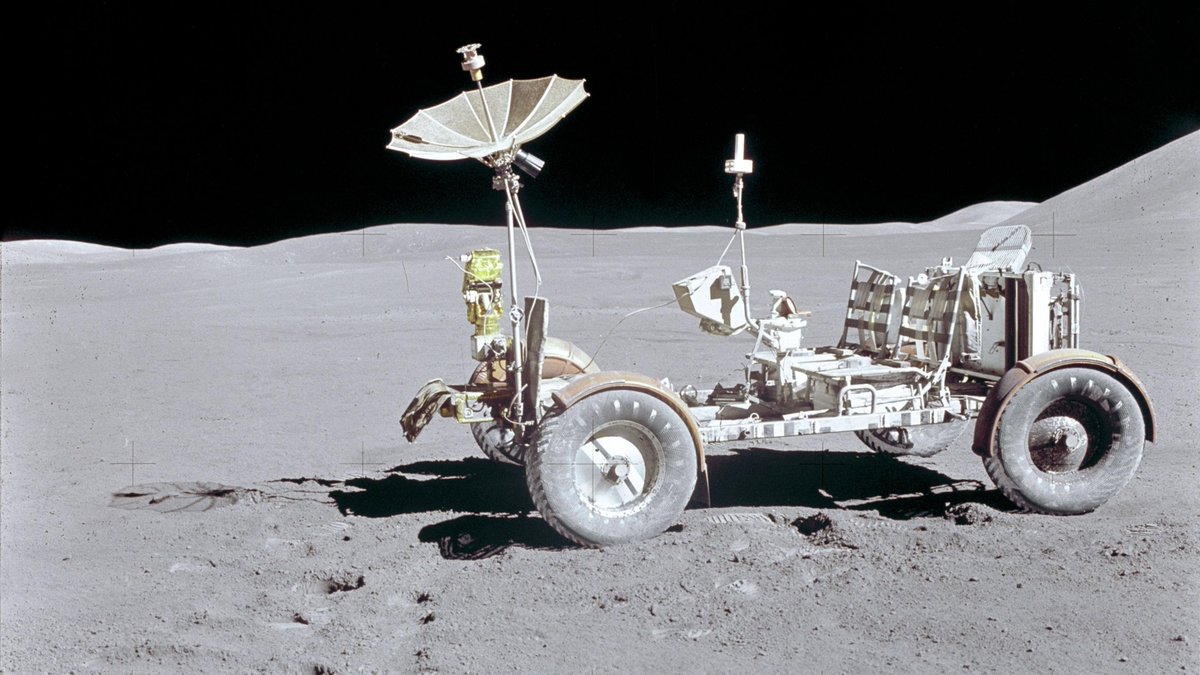 The Lunar Rover Vehicle is photographed alone against the lunar background during the Apollo 15 lunar surface extravehicular activity (EVA). Its wire-mesh wheels, designed to grip the powdery regolith, leave delicate tracks across the gray, cratered plain. The rover’s gold-foil