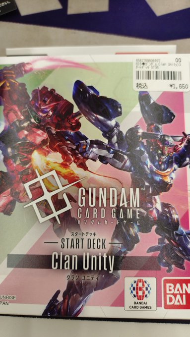 Boxed start deck for Gundam Card Game titled Clan Unity features artwork of red and blue mecha figures in dynamic poses against a gradient background with Japanese text labels Bandai logo and price tag of 1560 yen visible on the packaging