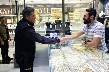 First image shows five men including police officers in uniforms sitting around a metal table outdoors on grass near parked cars and trees, engaged in conversation with one holding a cup. Second image depicts eight men standing in front of a building entrance with TAKSIT sign and decorative arches, some in police attire, posed for a group photo on a paved area with plants. Third image features three men seated on chairs near a wooden bench outside a brick building, two in police vests discussing. Fourth image captures two men shaking hands inside a jewelry store filled with gold displays and necklaces on counters, one in police uniform and the other in casual shirt.