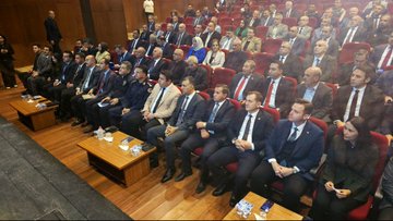 First image shows a conference room with a long white table covered in cloth, featuring a computer monitor, documents, glasses of water, and flower arrangements; three men in suits sit at the table, one with glasses and a mustache, another in a dark suit, and a third in a gray suit; Turkish flags and a banner reading BATTALGAZİ BELEDİYESİ hang in the background against wooden panels and stage curtains. Second image depicts rows of red chairs in an auditorium filled with men and women in formal business attire, including suits and dresses, seated and facing forward; small wooden tables with water bottles are placed in front of some rows; wooden walls and a Turkish flag are visible in the setting. Third image captures additional rows of seated attendees in suits and formal wear in the same auditorium, with some holding notebooks, water bottles on side tables, and the wooden interior with a flag in the background.