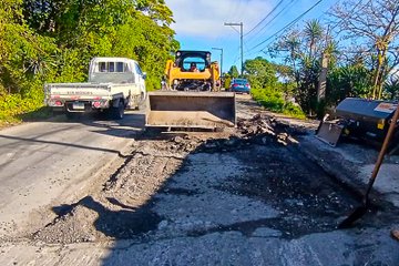 Multiple images show road maintenance scenes with workers in yellow shirts and helmets using shovels to handle asphalt on a roadside surrounded by green vegetation and utility poles. A yellow loader excavates damaged pavement, while another machine spreads asphalt. Traffic cones and a white truck are present, with clear skies overhead. Workers pour and level black asphalt material on the road surface. No watermarks visible.