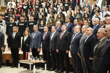 First image shows a man in a dark suit speaking at a podium with microphone in a conference room featuring banners for Turkiyenin En Buyuk Sendikasi and Arif Nihat Asya Nihai Asya alongside the Eğitim-Bir-Sen logo and a screen displaying Vefatının 50 Yılı. Second image depicts a man in a suit at a podium with a large projected portrait of Arif Nihat Asya wearing glasses and a red tie next to banners for Ercan Solusan and Arif Nihat. Third image captures a man in a gray suit speaking at a podium with Turkish and another flag banners for Turkiyenin En Buyuk Sendikasi and Eğitim-Bir-Sen plus a portrait of Arif Nihat Asya and text for Çukurova Solusan Mehmet Akif. Fourth image displays a large group of people including men and women in formal attire standing on a stage with a Turkish flag table with cups and microphones in a hall setting.