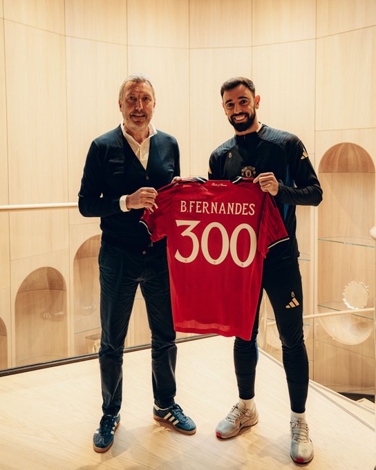 Bruno Fernandes holds up a United shirt with 'B. Fernandes 300' on the back alongside Jason Wilcox at Carrington.