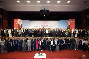 First image shows a man in a dark suit with a red tie standing at a white podium with microphones including one marked with a red logo, speaking towards the camera, with a large backdrop featuring the Turkish flag and a portrait of Recep Tayyip Erdoğan, blue panels on sides, and a red star element. Second image depicts a large group of about 50-60 people mostly men in dark suits and some women in formal attire standing in rows on a red carpeted area in a warmly lit hall with beige walls and geometric patterns, a small white table with flowers in front, and overhead lights. Third image captures a man in a dark suit with mustache sitting and holding a young girl in white top on his lap, another girl in pink headband and white shirt standing beside smiling, red seats around, flowers on a table nearby, and audience blurred in background. Fourth image shows a wide group of around 40 diverse participants including men and women in various formal outfits standing on a stage with red curtains, a central banner with Turkish emblem and text, flanked by large Turkish flags and portraits of Recep Tayyip Erdoğan, wooden floor, and a small table with flowers below.