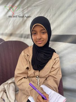 First image shows a young girl with brown skin wearing a black hijab and beige striped long-sleeve shirt sitting on a brown rattan chair holding a purple pen and writing in an open notebook on her lap with Arabic script visible. Background includes a beige tent-like structure and another chair. Overlay text reads We Will Read Again with heart and book emojis. Second image shows the same girl smiling with closed-mouth expression standing in front of a blue wall painted with green heart book logo and We Will Read Again text plus drawings of numbers 1 and letters X C in white chalk and Arabic script.