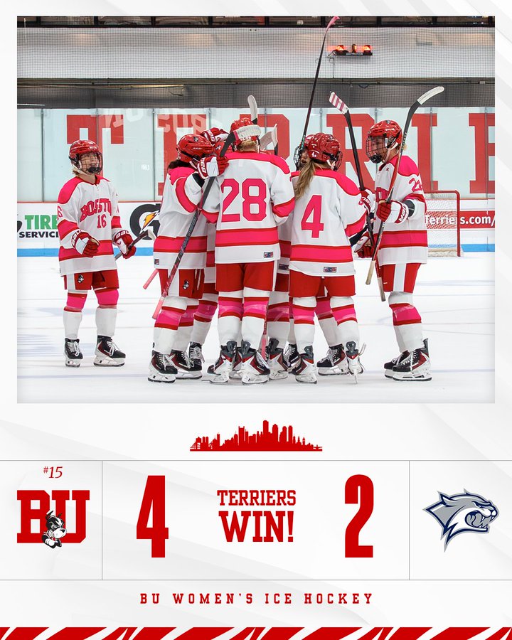 Group of female hockey players in red and white jerseys numbered 16 28 4 standing together on ice rink holding sticks some wearing helmets with Terrier logo visible in background scoreboard graphic at bottom reads BU 4 Terriers win 2 with skyline icon and opponent logo.
