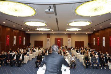 First image shows a man in a suit speaking at a podium with banners reading 47 Baskanlar Kurulu Toplantisi 23-26 Eylul Antalysi and TOC BIR-SEN logos on a stage backdrop. Second image depicts a conference room with attendees seated at round tables under ceiling lights facing a stage with Turkish flags and TOC BIR-SEN signage. Third image captures a man in a suit gesturing from behind a podium in a room with projected screen overhead lights and audience seated at tables with Turkish flags on walls. Fourth image features a large group of people standing together in formal attire in front of a stage with TOC BIR-SEN banners Turkish flags and event signage.