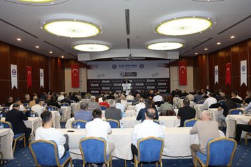 First image shows a man in a suit speaking at a podium with banners reading 47 Baskanlar Kurulu Toplantisi 23-26 Eylul Antalysi and TOC BIR-SEN logos on a stage backdrop. Second image depicts a conference room with attendees seated at round tables under ceiling lights facing a stage with Turkish flags and TOC BIR-SEN signage. Third image captures a man in a suit gesturing from behind a podium in a room with projected screen overhead lights and audience seated at tables with Turkish flags on walls. Fourth image features a large group of people standing together in formal attire in front of a stage with TOC BIR-SEN banners Turkish flags and event signage.