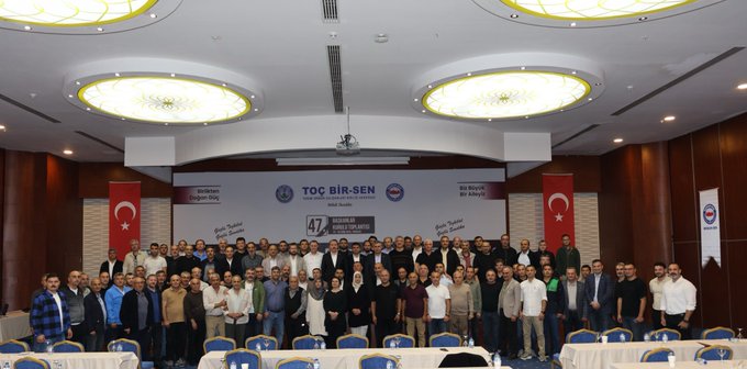 First image shows a man in a suit speaking at a podium with banners reading 47 Baskanlar Kurulu Toplantisi 23-26 Eylul Antalysi and TOC BIR-SEN logos on a stage backdrop. Second image depicts a conference room with attendees seated at round tables under ceiling lights facing a stage with Turkish flags and TOC BIR-SEN signage. Third image captures a man in a suit gesturing from behind a podium in a room with projected screen overhead lights and audience seated at tables with Turkish flags on walls. Fourth image features a large group of people standing together in formal attire in front of a stage with TOC BIR-SEN banners Turkish flags and event signage.