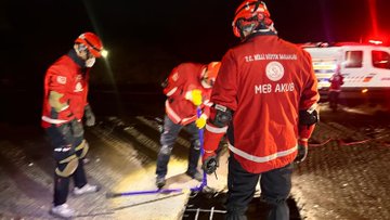 Group of rescuers in red uniforms and yellow helmets standing together on rocky terrain at night during a disaster drill in Kastamonu. Another image shows a rescuer in red gear lying on the ground near a manhole cover with team members surrounding the scene. Third image depicts rescuers in red outfits working near a white ambulance marked with Turkish Ministry of National Education and MEB AKUB logos on a debris-strewn area at night.