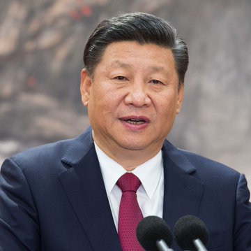 A man with short dark hair wearing a dark blue suit red tie and white shirt stands at a podium speaking into two black microphones against a blurred rocky reddish background. The first image shows Xi Jinping in formal attire addressing an audience. The second image depicts Earth from space with the North American continent illuminated by city lights at night under a glowing yellow semi-transparent dome overlay extending over the region with a sunrise effect on the horizon.