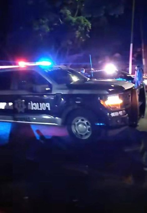 Nighttime scene with a black police truck displaying POLICIA on side with blue and red flashing lights activated parked on a wet street surrounded by trees and streetlights multiple vehicles and officers visible in background second image shows a street intersection at night cordoned off with yellow tape barriers across road several cars parked nearby including white sedans and a truck under streetlights with trees and buildings in dim lighting