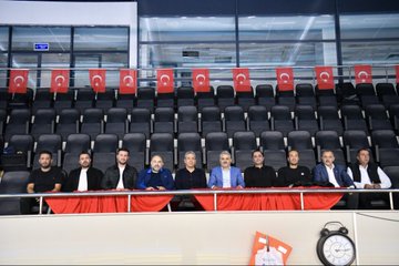 First image shows swimming pool with blue water and swimmers in action, Turkish and Palestinian flags hanging above, banner reading Özgür Filistin Free Palestine, audience seated in stands. Second image depicts group of men in suits and casual attire sitting on red-draped bench in front of empty seats with Turkish flags, clock and sign visible. Third image captures line of young athletes in yellow uniforms holding Turkish and Palestinian flags, walking along poolside in sports hall with banner of mayor. Fourth image features young female swimmers diving from starting blocks into pool, wearing swim caps and suits, lane markers and officials present.