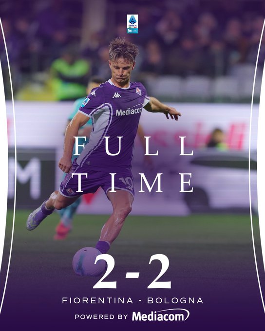 A soccer player in a purple and white ACF Fiorentina jersey with Mediacom sponsor logo dribbles a soccer ball on a green field during a match against Bologna wearing green and blue kit visible in background stadium crowd watches player has blonde hair and wears purple cleats scoreboard overlay shows Full Time and 2-2 score text powered by Mediacom at bottom