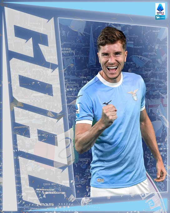 Sky blue bordered graphic with overlaid text GOAL in white bold letters at top and bottom, central image of young male athlete with short brown hair smiling widely and raising right fist in celebration while wearing light blue soccer jersey with white collar, sponsor patches, and eagle emblem on chest, white shorts, against blurred stadium background.