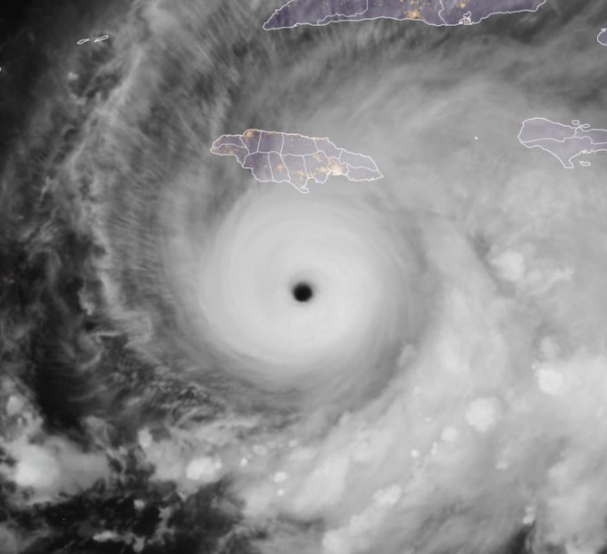 Satellite image displays a well-defined hurricane eye surrounded by a spiral band of clouds and thunderstorms over the Atlantic Ocean near the Caribbean islands including Jamaica and surrounding landmasses outlined in white.